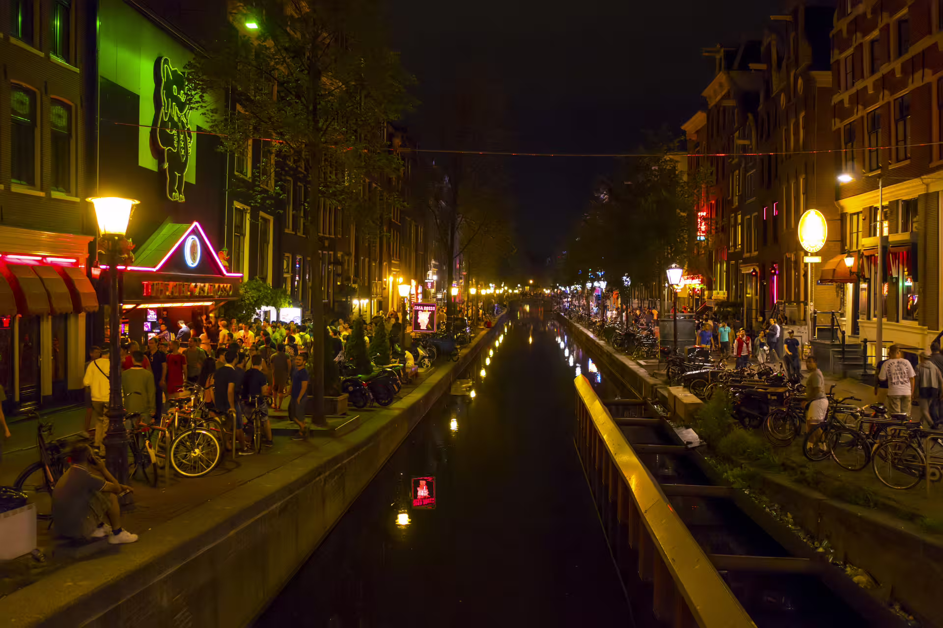 Night canal view in Amsterdam Red Light District with neon lights and crowds, 1-day walking tour audioguide route