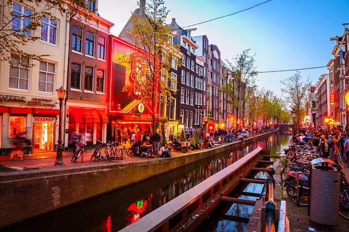 Amsterdam Red Light District canal at dusk with crowded streets, neon lights, and traditional Dutch buildings