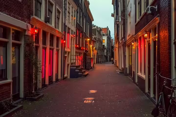 Narrow Amsterdam alley with red-lit doorways and brick buildings at dusk