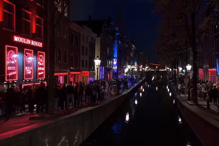 Amsterdam Red Light District canal at night with neon-lit venues and crowds, seen on a private guided tour