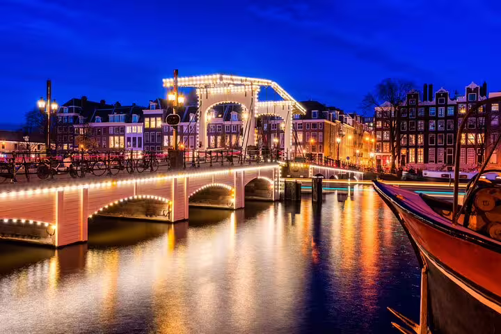 Illuminated Magere Brug drawbridge over Amsterdam canal at night with glowing reflections on water
