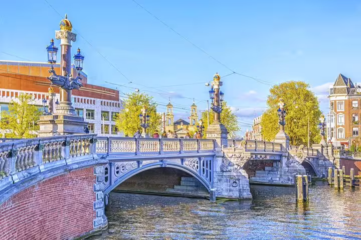 Ornate blue stone bridge with decorative lampposts over Amsterdam canal on a sunny day