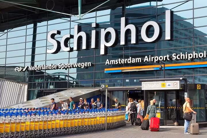 Amsterdam Airport Schiphol entrance with travelers and luggage carts, book Amsterdam to Schiphol private transfer