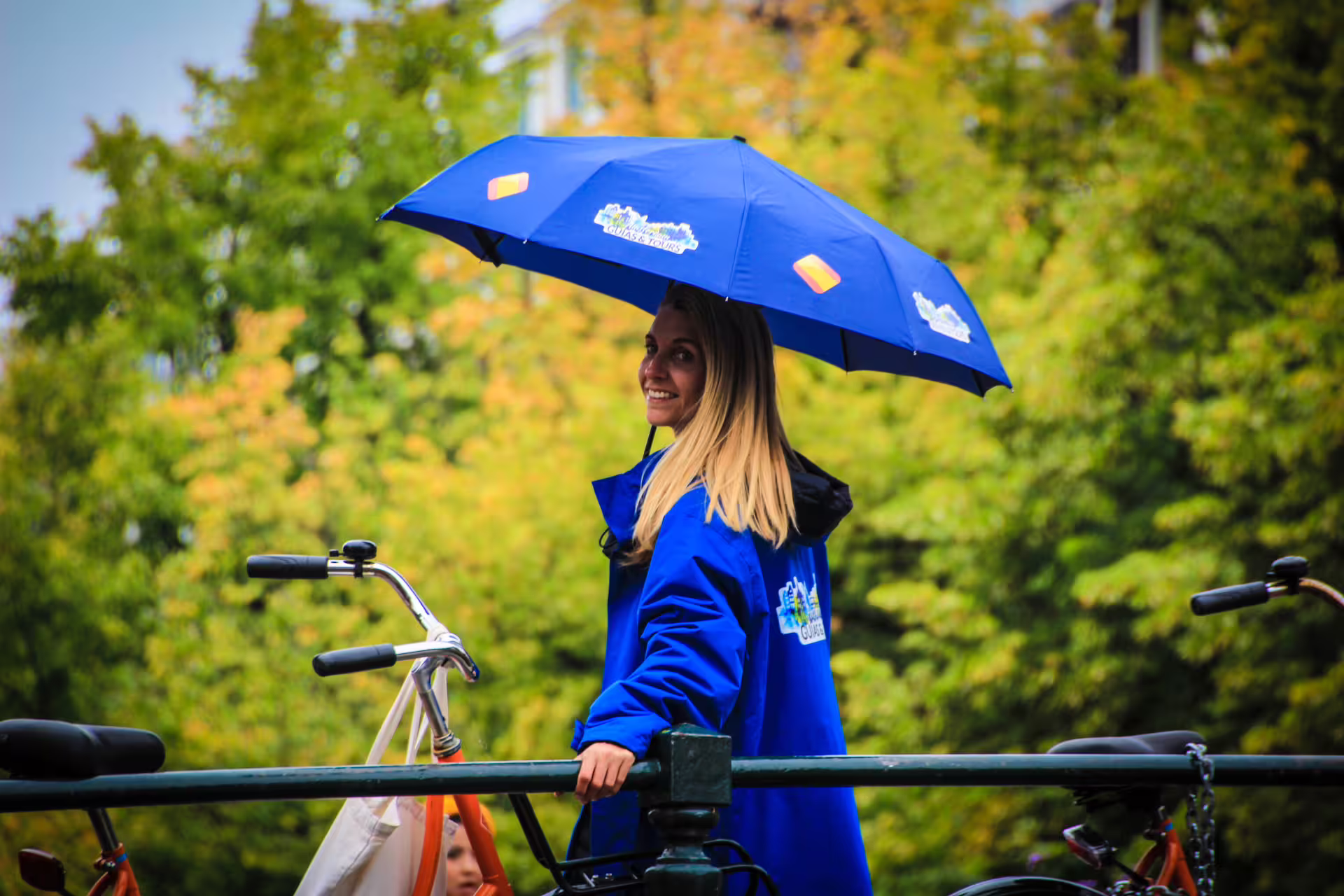Guide in blue coat with branded umbrella standing by a bike on an Amsterdam canal tour, offering a unique Dutch experience.