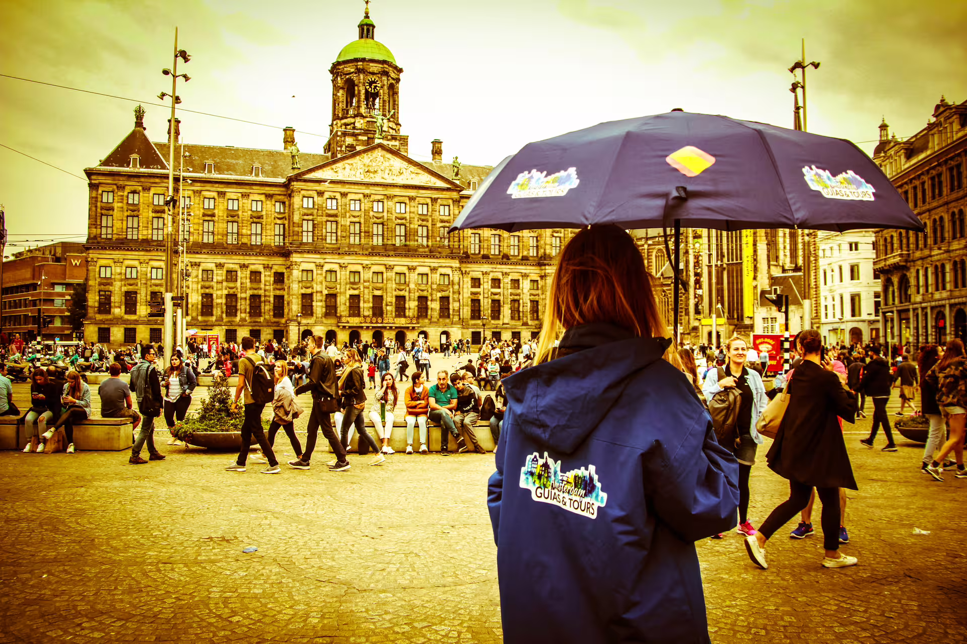 Tour guide with umbrella leading a group in busy Dam Square, Amsterdam, highlighting walking, biking, and cruising tour.