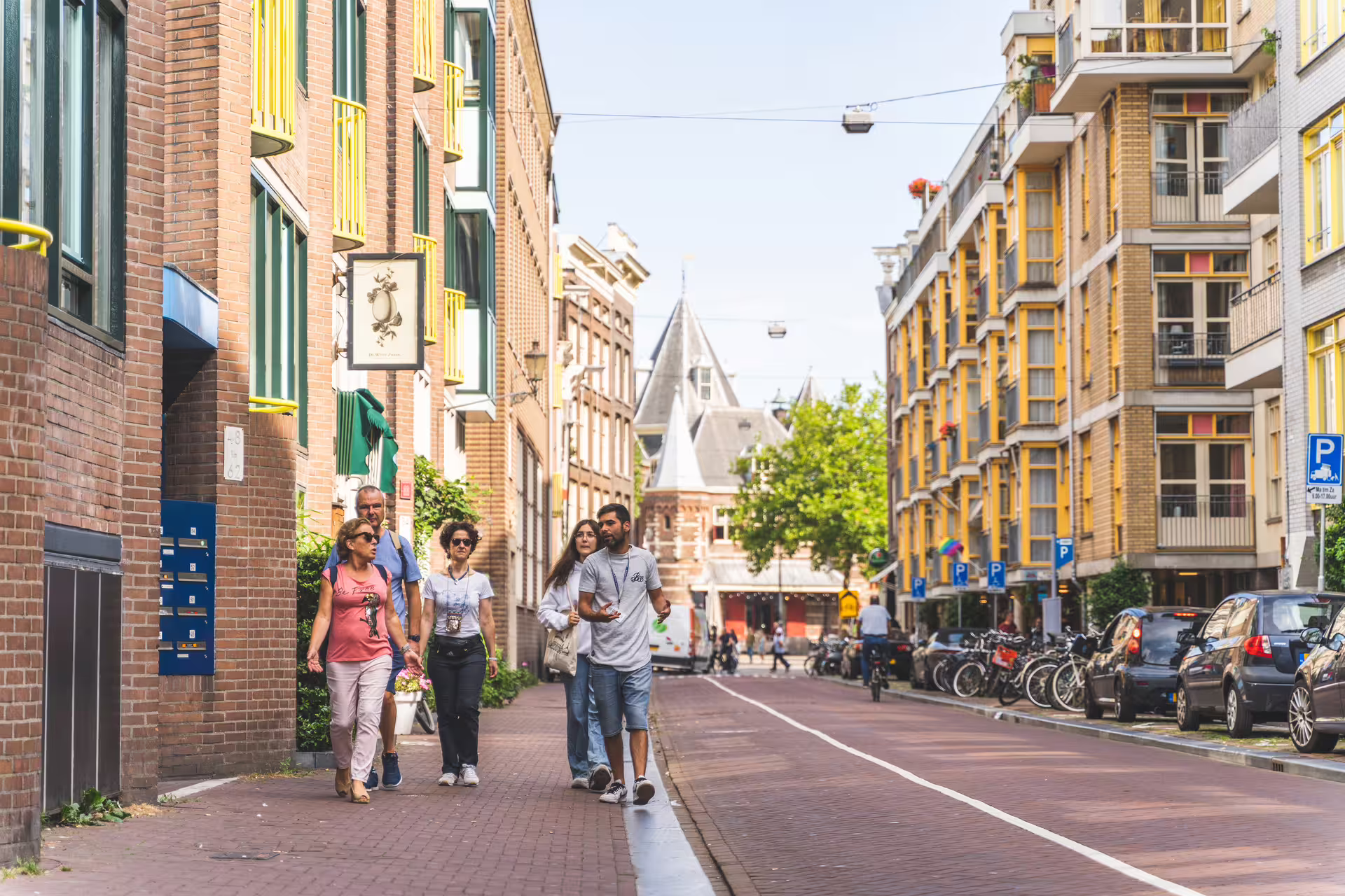 Group enjoying a sunny Amsterdam walking tour with cheese tasting, exploring vibrant streets and picturesque architecture.