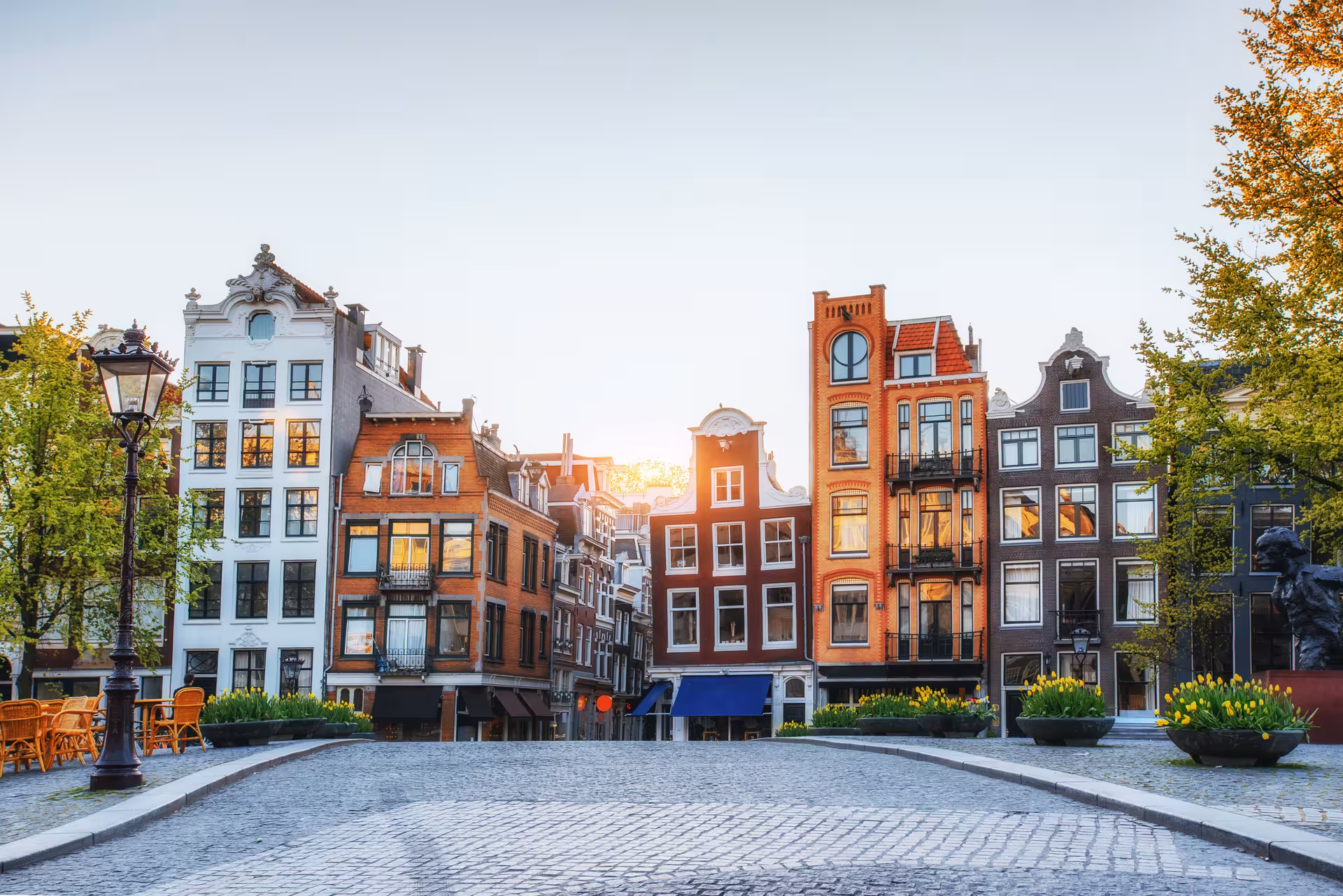 Cobblestone square surrounded by colorful Dutch canal houses at golden hour in Amsterdam