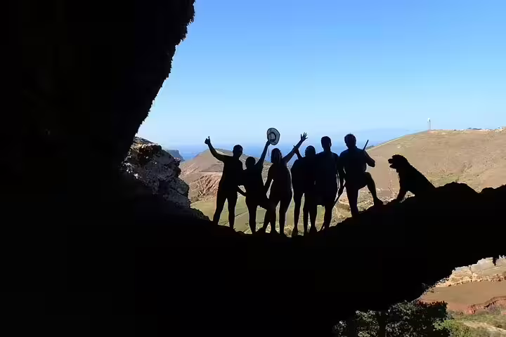 Silhouetted hikers celebrate in a cave on the scenic Ana Ferreira Caves & Peaks Trek with panoramic mountain views.