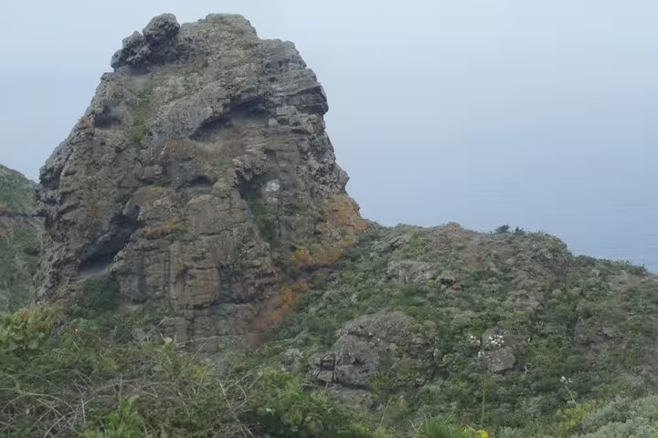 Majestic rocky formation in Anaga Rural Park, Tenerife, surrounded by lush greenery and misty skies.