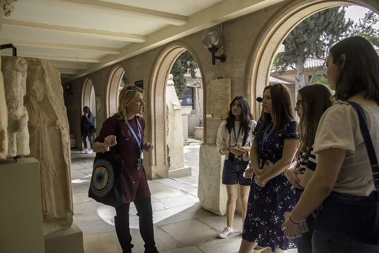 Guide explaining marble reliefs at the Ancient Corinth museum arcade during a guided full-day tour from Athens