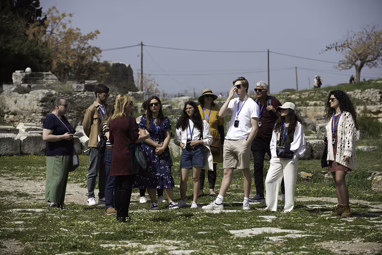 Travelers listening to guide among Ancient Corinth ruins on a full-day guided tour combining Corinth and Nafplion