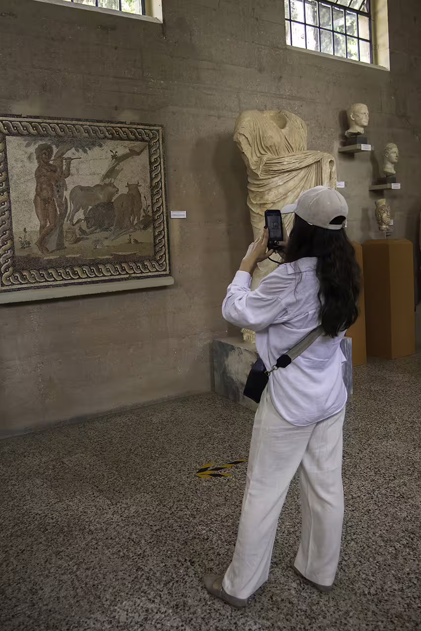Tourist taking photo of Roman mosaic and marble statue in Ancient Corinth museum on Nafplion day trip from Athens
