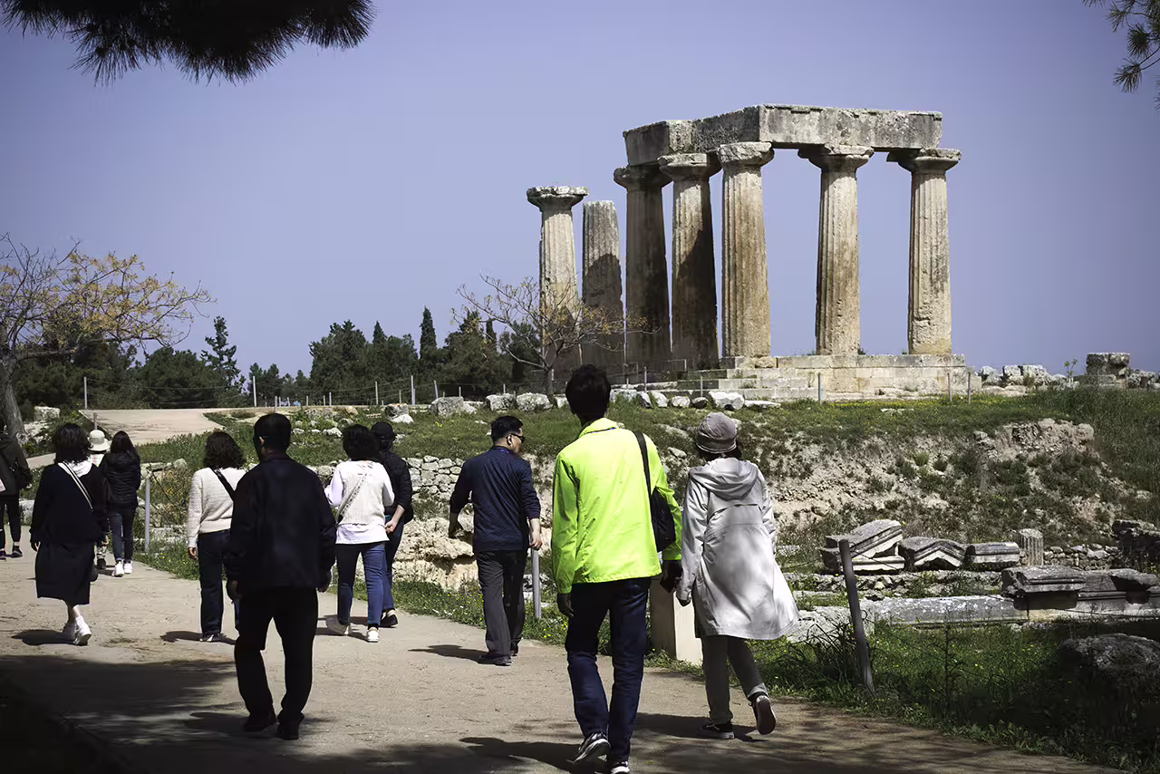Tour group walking to Ancient Corinth Temple of Apollo ruins on guided full-day trip from Athens to Nafplion