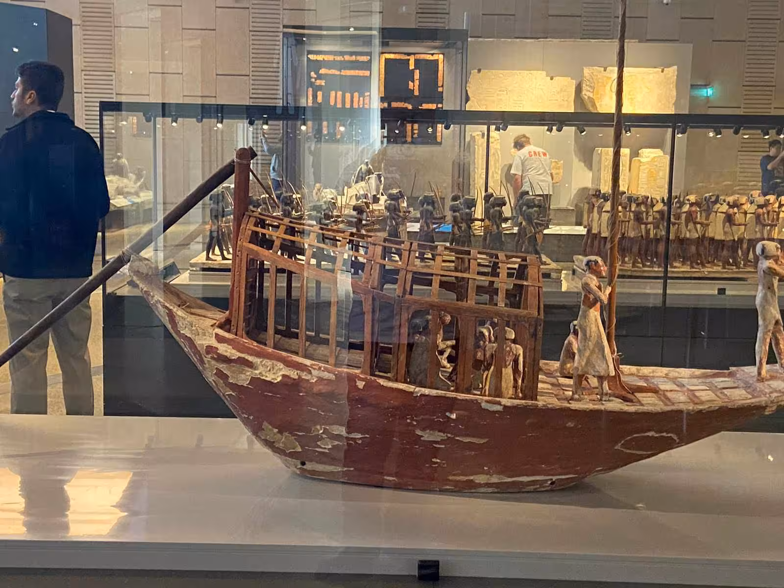 Ancient Egyptian wooden boat model with crew figures inside the Grand Egyptian Museum on a guided tour