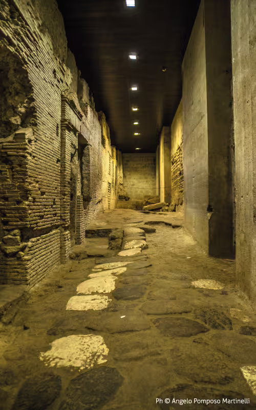 Illuminated underground Roman street on the Ancient Naples Buried Path tour, showcasing brick walls and worn stone paving