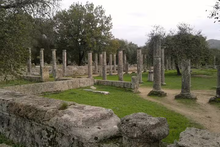 View of Ancient Olympia ruins with standing columns and grassy paths, featured on Olympia full day tour