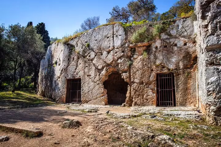 Ancient rock-cut tombs with iron gates carved into a limestone cliff in Athens, Greece
