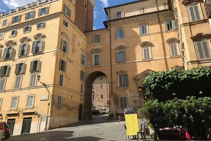 Ancient Roman archway between yellow ochre buildings on a cobblestone street in Rome