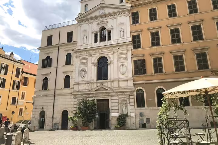 White Baroque church facade on cobblestone piazza in Ancient Rome surrounded by ochre buildings