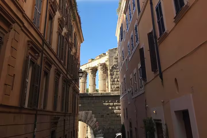 Narrow Roman street with ancient temple columns and archway visible between historic buildings in Rome