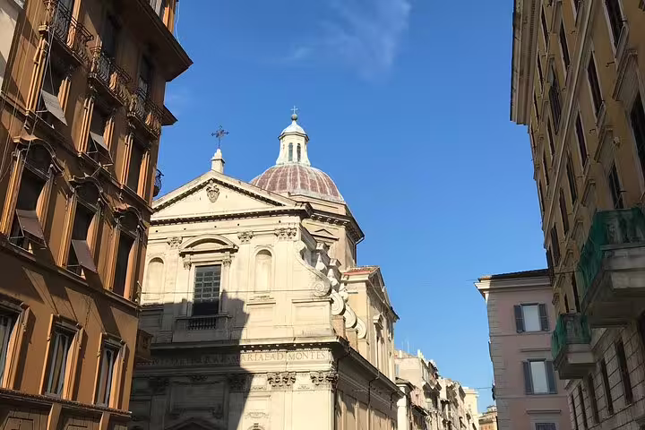 Baroque church dome rising above narrow Rome street flanked by classical Italian buildings under blue sky