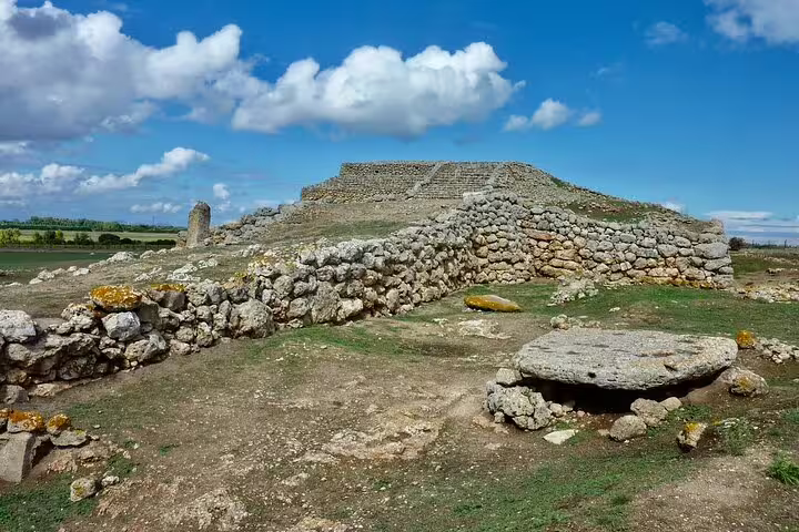 Ancient stone ruins with stepped pyramid structure under blue sky in open landscape