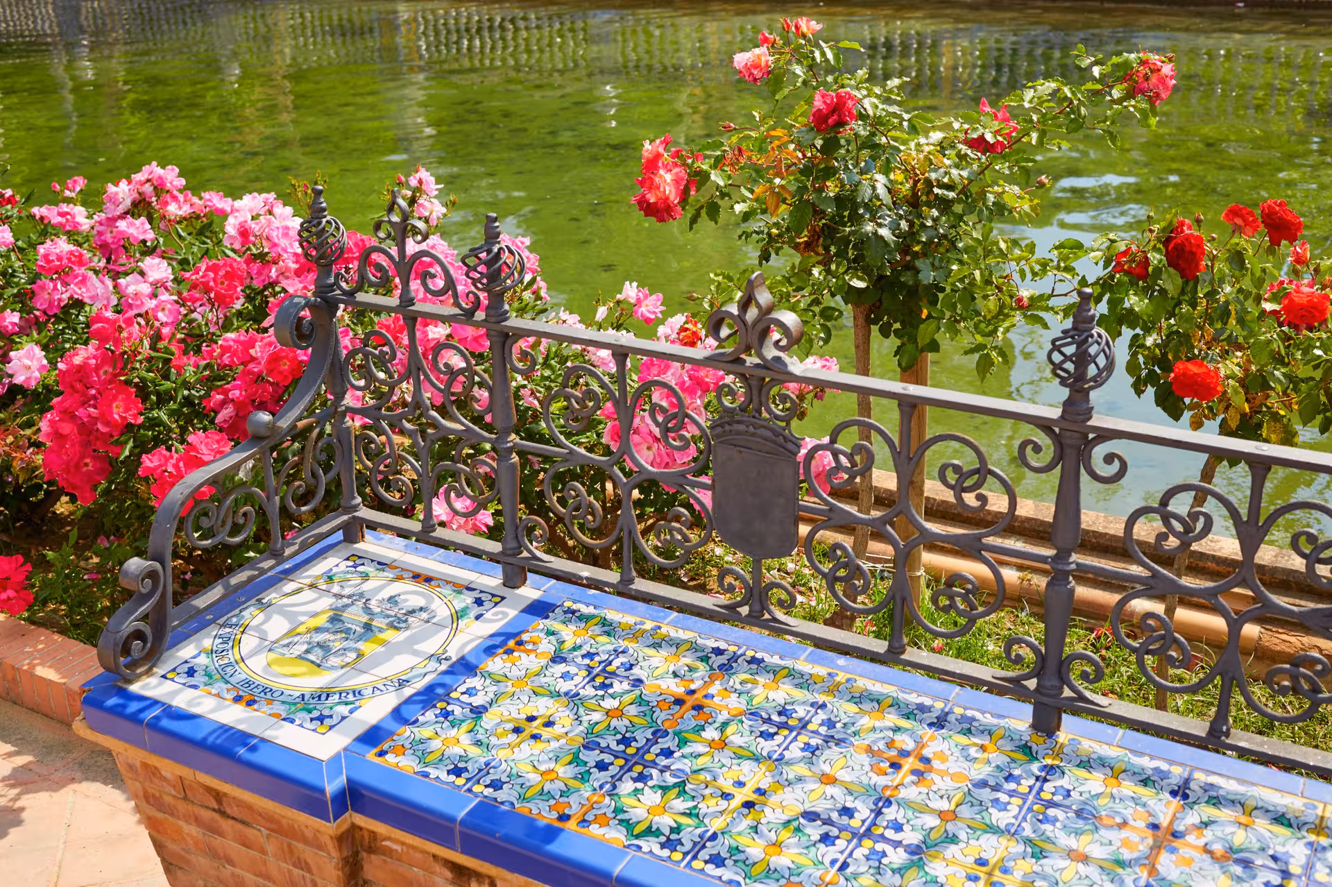 Colorful tiled bench with ornate ironwork and blooming roses at a serene Andalusian garden.