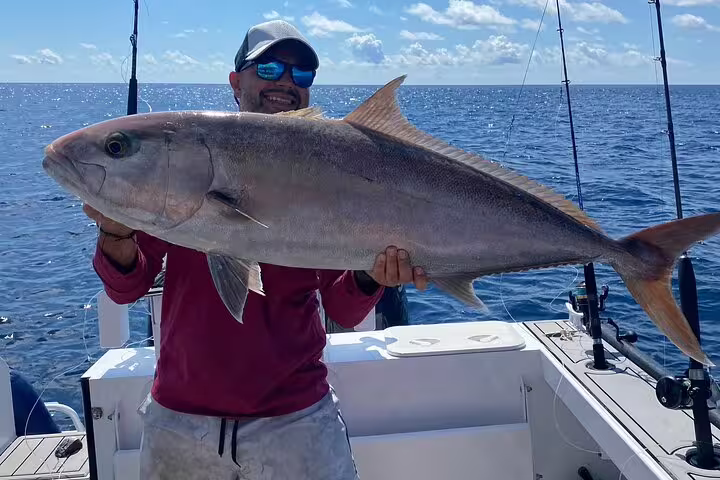 Angler proudly displays large fish aboard a Seychelles fishing charter on a sunny day.