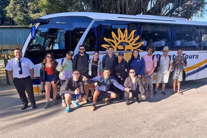 Group of travelers smiling in front of a tour bus, ready for a shared transfer from Angra dos Reis to Rio de Janeiro.