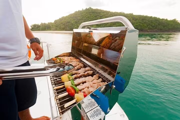 A chef grills skewers with fresh vegetables and meat on a boat, offering a delicious barbecue experience in Ilha Grande.