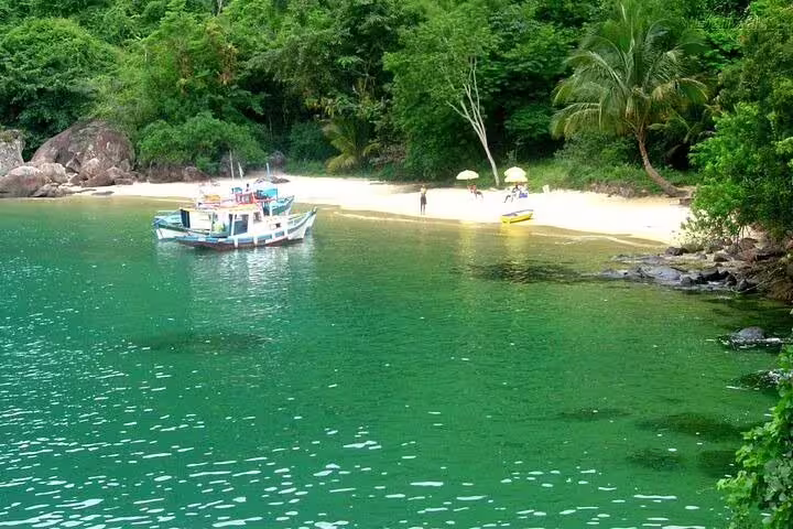Scenic view of a boat anchored near a secluded beach on the Angra & Ilha Grande boat tour with lush greenery.