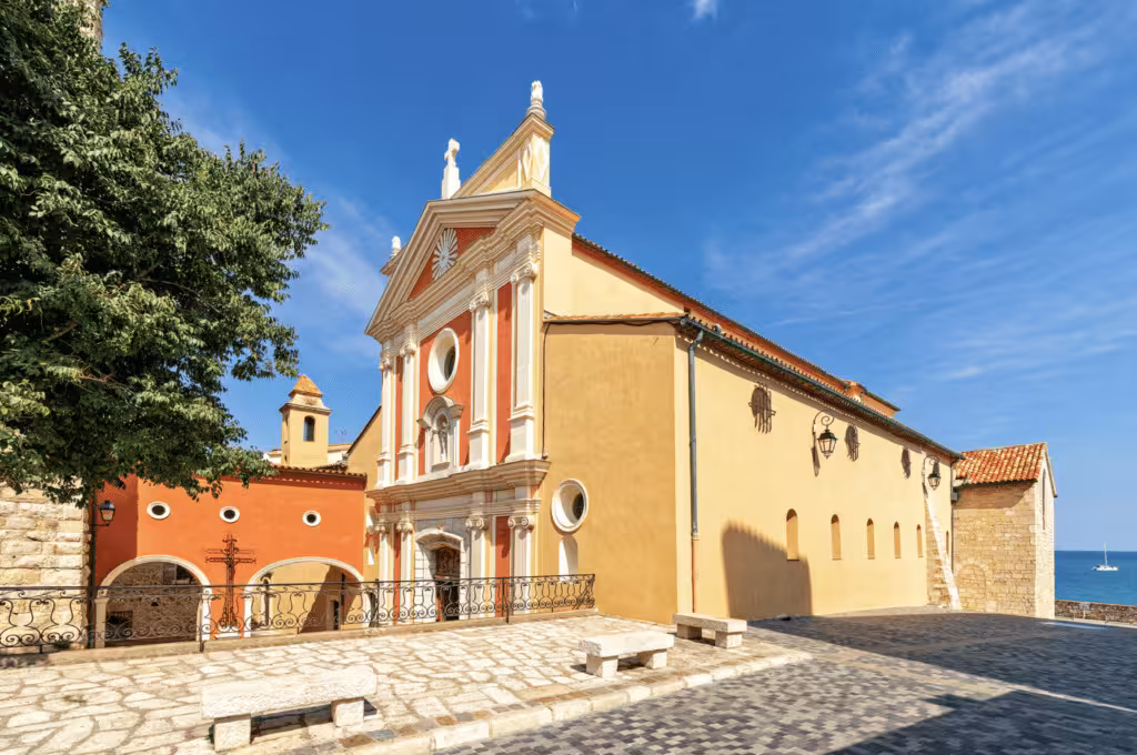 Colorful Baroque church with red and yellow facade on cobblestone square in Antibes, French Riviera