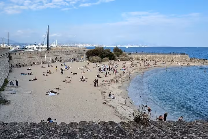 Sandy beach at Antibes old town fortifications with sunbathers and calm Mediterranean Sea on French Riviera