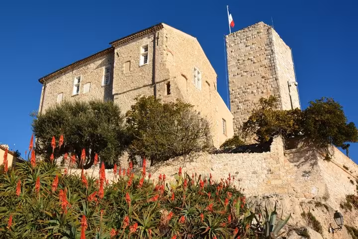 Historic Château Grimaldi castle with red flowers and French flag in Antibes, France