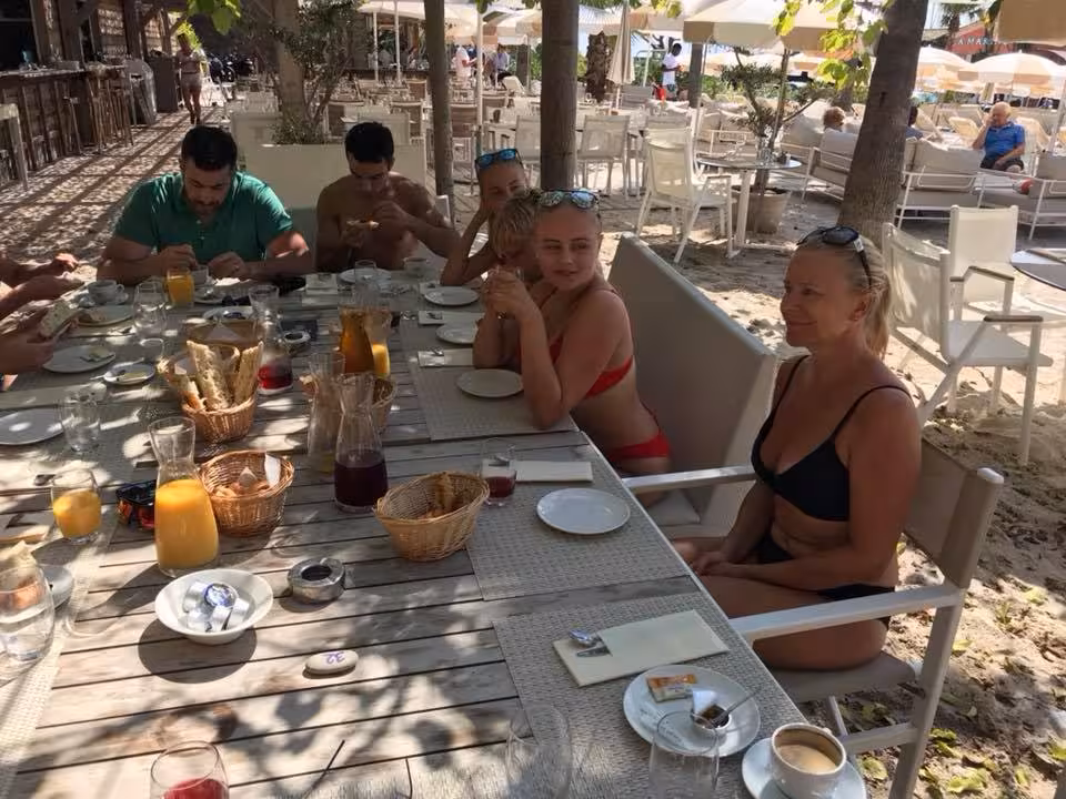 Group enjoying outdoor sea breakfast at beachside restaurant in Antibes, with bread baskets and juice on table