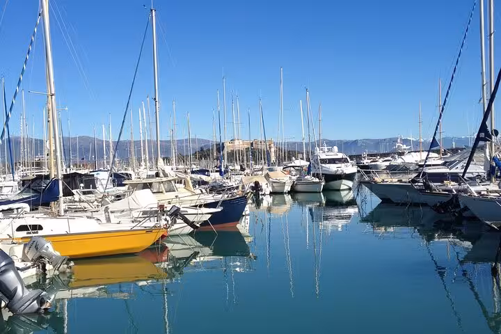 Sailboats and yachts moored in Antibes marina with calm turquoise water and mountains in background