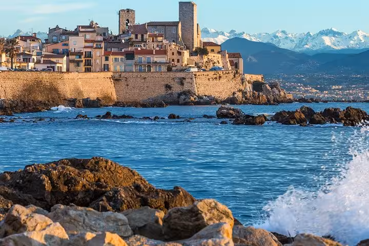 Rocky coastline of Antibes old town with medieval walls, colorful buildings, and snow-capped Alps in background