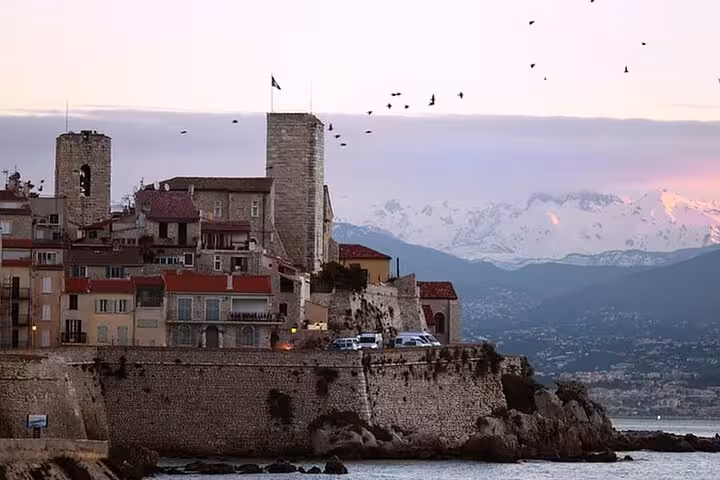 Historic Antibes old town fortified walls at dusk with snow-capped Alps and birds in background