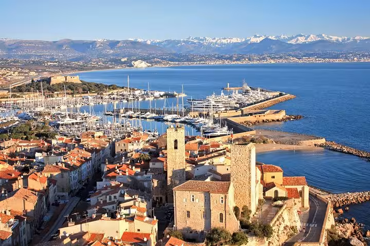 Aerial view of Antibes old town, marina with yachts, and French Riviera coastline with snow-capped Alps backdrop