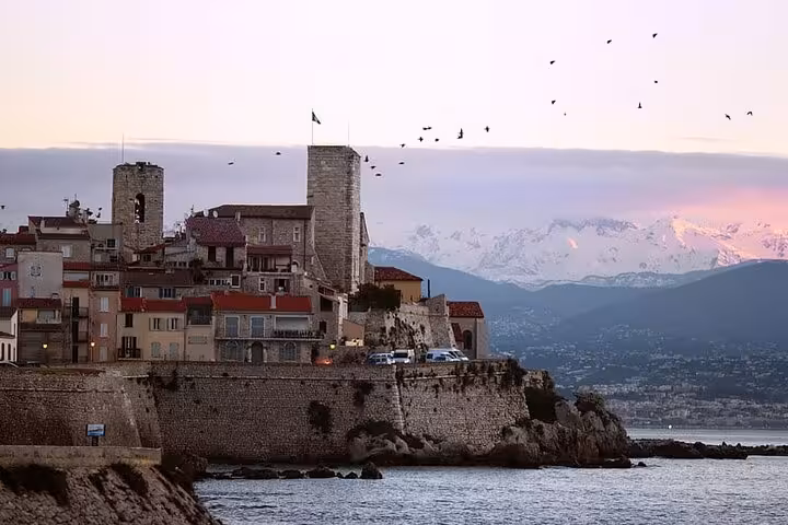 Historic old town of Antibes with medieval sea walls, snow-capped Alps and birds at dusk, French Riviera