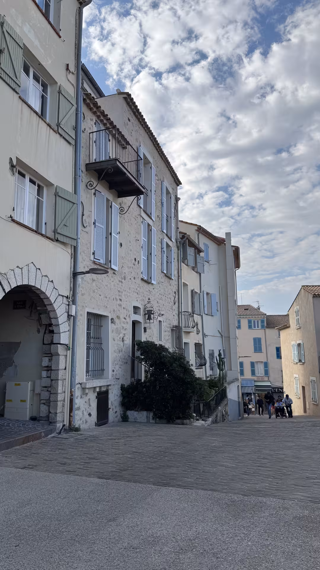 Historic stone buildings with blue shutters and arched gateway in Antibes old town, French Riviera