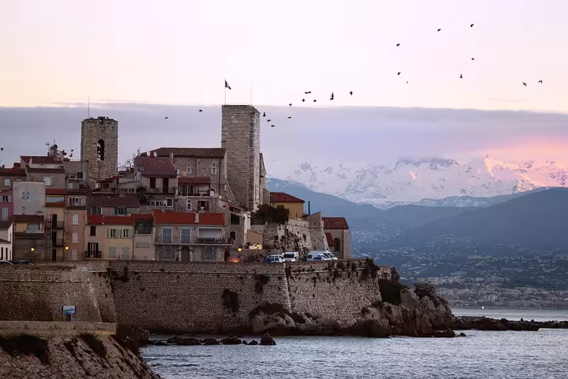 Medieval walled old town of Antibes at dusk with snow-capped Alps and birds flying overhead