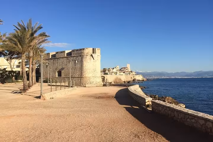 Ancient stone ramparts of Antibes old town along the French Riviera coastline with palm trees