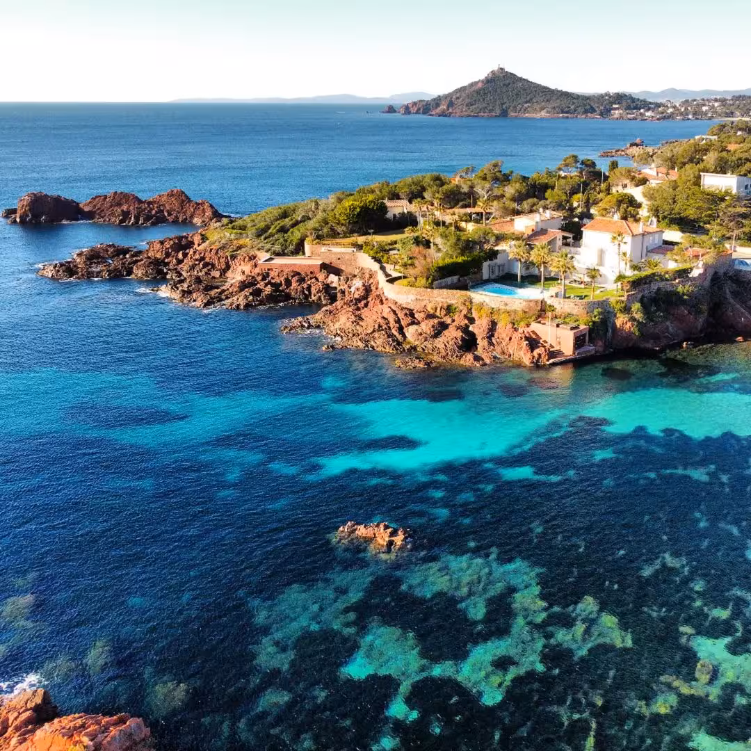 Aerial view of turquoise Mediterranean waters and red rock coastline near Antibes with luxury villas
