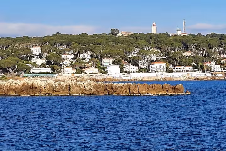 Rocky coastline of Antibes with white villas, pine trees, and a lighthouse on the French Riviera