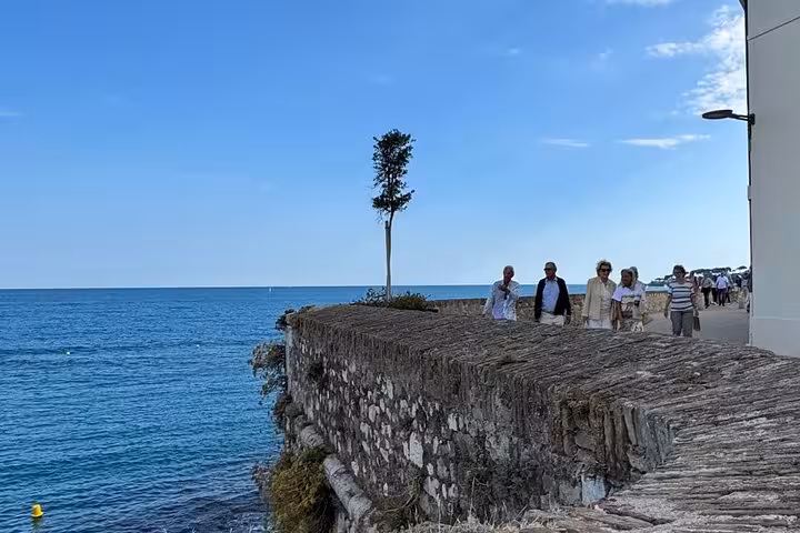 Visitors walking along a historic stone sea wall overlooking the blue Mediterranean in Antibes, French Riviera