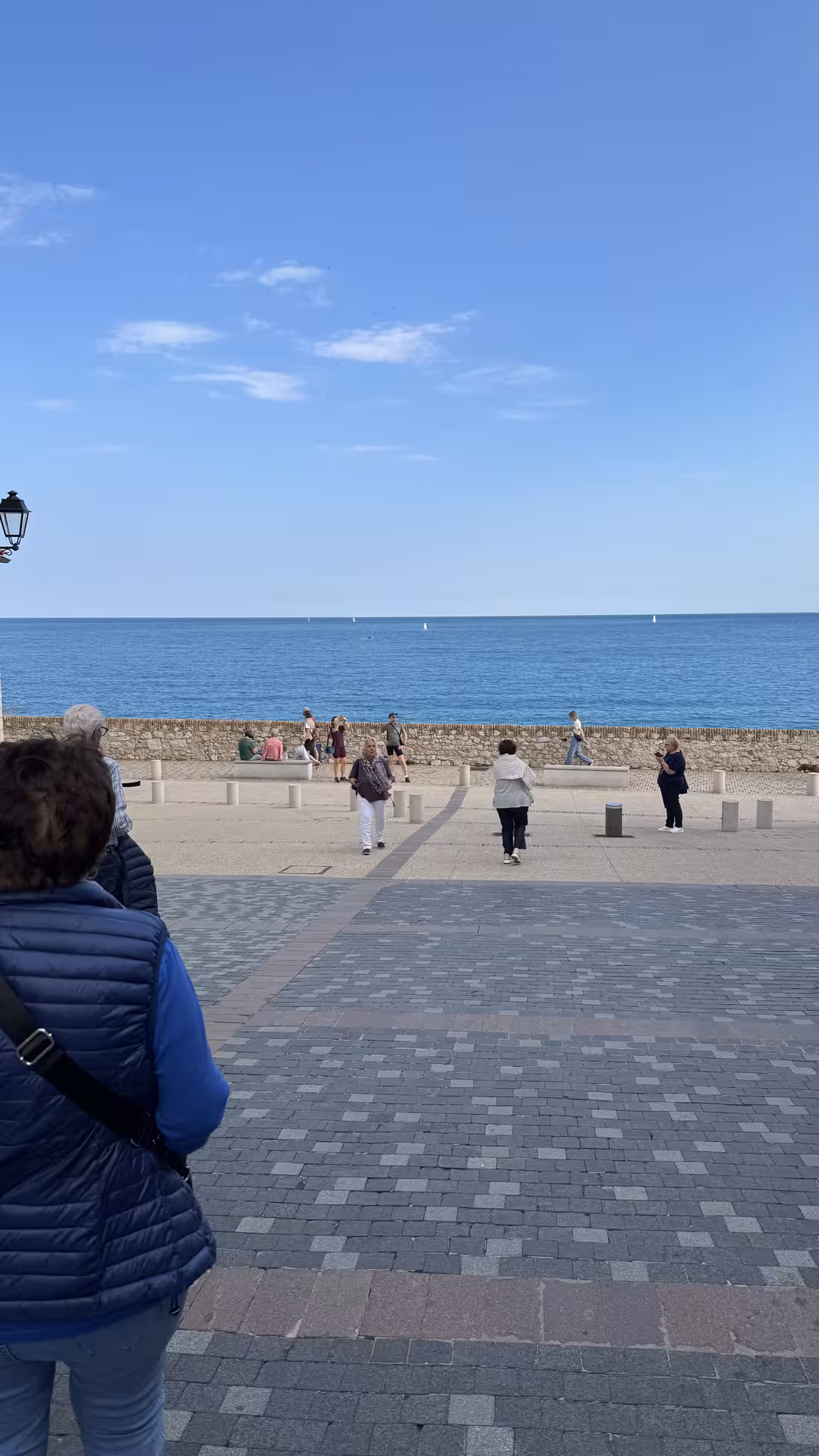 Tourists strolling along Antibes seafront promenade with calm blue Mediterranean Sea views