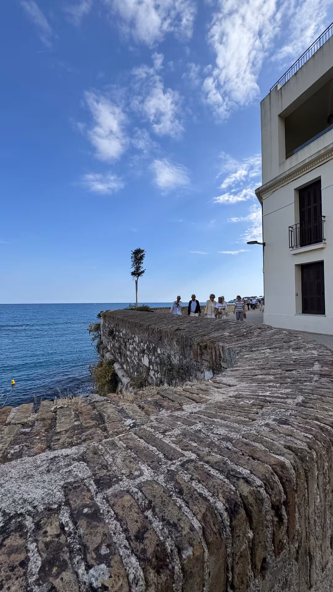 Ancient stone ramparts along the Antibes coastline with Mediterranean Sea views and strolling tourists