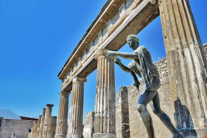 Bronze Apollo statue among ancient Roman columns at Pompeii ruins with blue sky backdrop