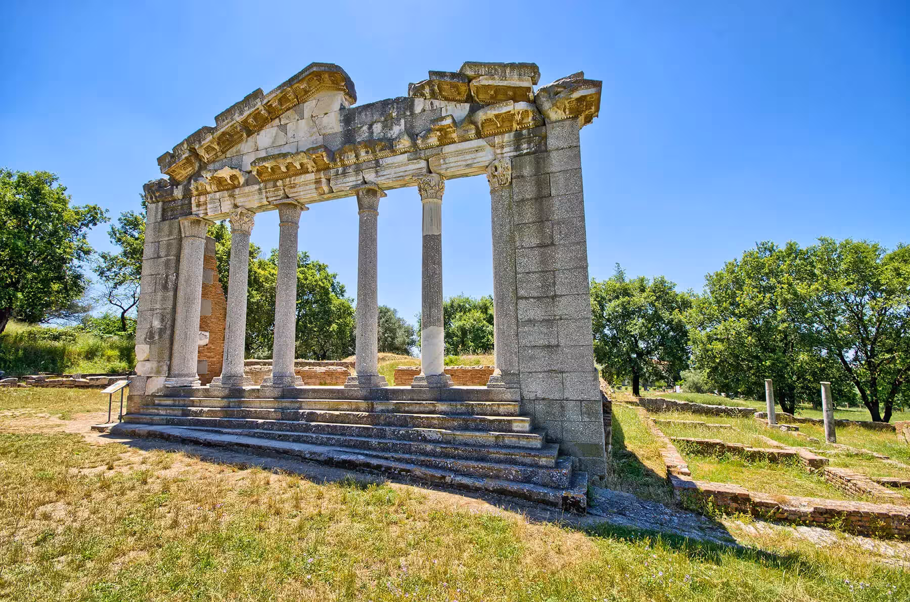 Explore ancient ruins in Apollonia, showcasing historic Greek architecture amidst lush greenery on a sunny day.